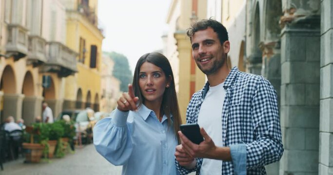 Young happy romantic couple of tourist using applications on a smartphone for checking new places to visit together while sightseeing  in old city center during holidays trip.