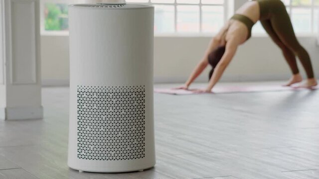 Air purifier in cozy white Living room for filter and cleaning removing dust PM2.5 HEPA at home with woman exercise yoga in background,for fresh air and healthy life,Air Pollution Concept