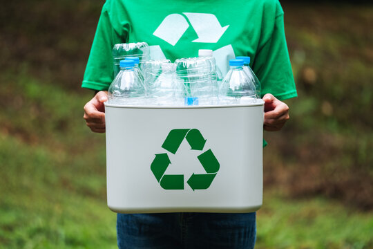 A woman holding a recycle bin with plastic bottles in the outdoors