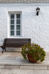 Fototapeta na wymiar White washed stone wall, wooden bench and potted flowers in Greece.