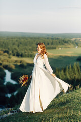 Fototapeta na wymiar Bride with a bouquet of dried flowers walking in nature. Boho style wedding in autumn.