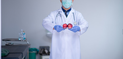 A male doctor with a stethoscope holds a red apple on a gray background