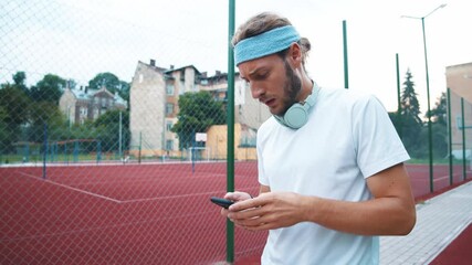 Tired fitness trainer wearing headband and earphones using smartphone sports application typing messages resting walking on the racetrack. - Powered by Adobe