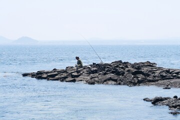 A lonely man sits on the rocks and fishes in the middle of the sea