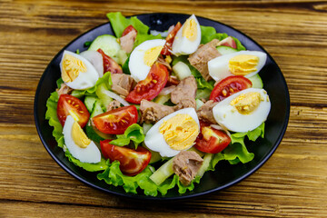 Tasty tuna salad with eggs, lettuce and fresh vegetables on wooden table
