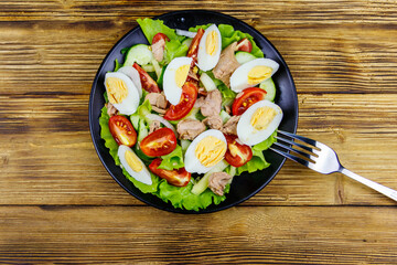 Tasty tuna salad with eggs, lettuce and fresh vegetables on wooden table. Top view