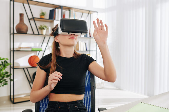 Teenage girl spending weekend at home and playing game in virtual reality glasses