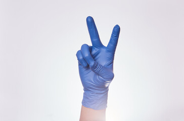 Mano de hombre formando la señal de paz y amor con guantes de nitrilo en fondo blanco.