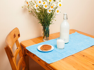 Simply stylish wooden kitchen with bottle of milk and glass on table, summer flowers camomile, healthy foog moring concept