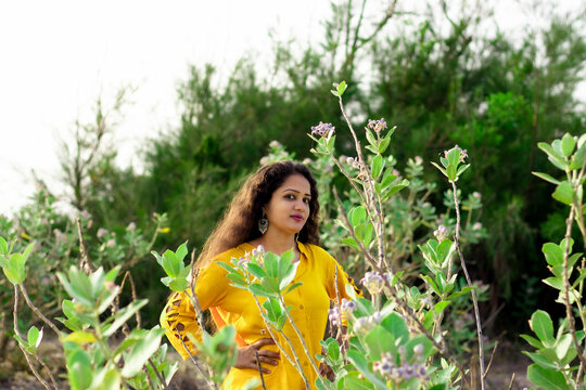 A beautiful Asian woman is standing near the Aak, Madar (Calotropis gigantea) tree wearing a yellow top and selective focus points background, outdoors portrait