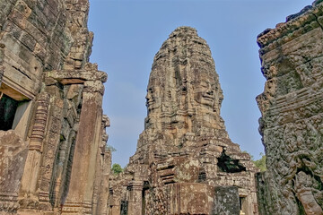 Against the background of the blue sky, the top of the temple. Human faces with smiles are carved...