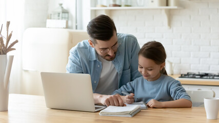 Caring young dad helping small primary pupil kid daughter preparing school homework, sitting...