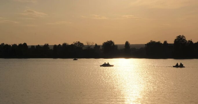 Calm natural video of a lake, river, canal with boats, coracle, paddle boats, coble, slalom, dory with people on a beautiful sunset with treason a background in 4k slow motion panorama, water shining