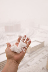 A male hand holds a freshly fallen snowball. View of real snow with selective focus. Snow falling from the sky on a blizzard background. Heavy snowfall and a view from the heights of the city.
