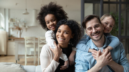 Portrait of happy multiracial couple enjoying sweet family moment with adorable little mixed raced daughters at home. Smiling cute small stepsisters cuddling cheerful parents, looking at camera. - Powered by Adobe