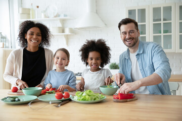 Portrait of happy african american woman and european man preparing vegetarian healthy fresh salad food with adorable mixed race children girls in modern kitchen, multiracial family healthcare hobby.