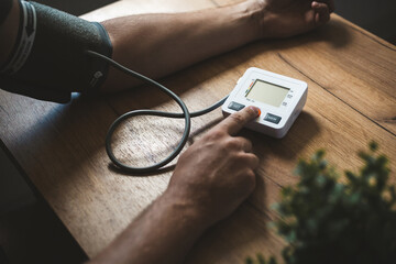 Man measures his blood pressure behind the wooden table