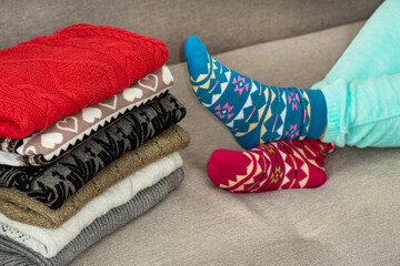 Stack of knitted colorful clothes . Women's legs in different beautiful socks. Female legs in socks on a stack of warm clothes. The concept of winter clothing.