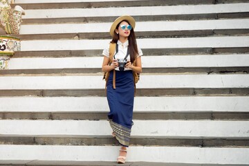 Obraz premium Young woman traveling with holding camera and backpack in wat arun Bangkok Thailand