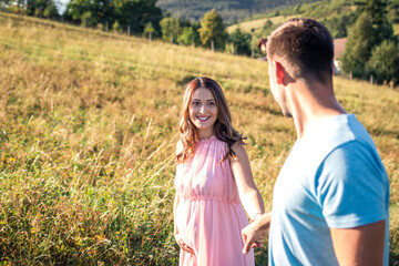 Young couple expecting baby holding hands. Smiling pregnant woman following her husband
