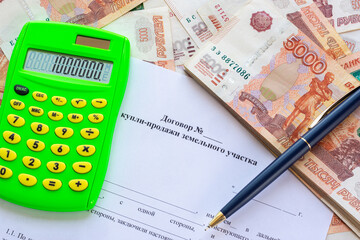 The contract for the sale of the land plot contains a calculator, a wad of money and a pen