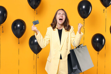 Happy young woman 20s wearing suit jacket hold package bags with purchases after shopping credit...
