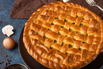 Tasty mushroom pie on the black plate with some cutlery champignons near. Big pie isolated on gray background. Brown napkin near the pie. Restaurant's recipe for everyone. Healthy food.