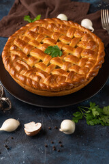 Tasty mushroom pie on the black plate with some cutlery champignons near. Big pie isolated on gray background. Brown napkin near the pie. Restaurant's recipe for everyone. Healthy food.