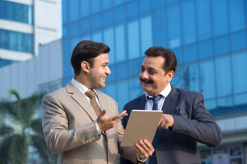 Two Indian businessmen using digital tablet outdoors in city