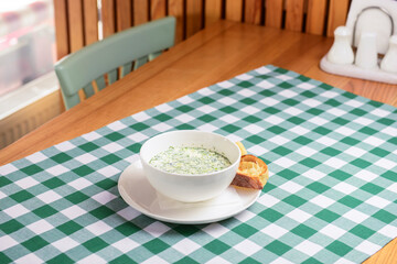 Popular spring or summer cold soup okroshka. Okroshka in a white bowl, bread and herbs on a table.