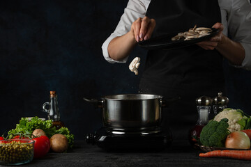 Chef cooking tasty soup with champignons. Chef puts mushrooms to the pan. Girls hands keep plate...
