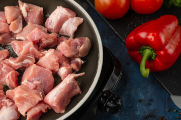 Frying pan with fresh meat isolated on dark black background with red pepper and tomatoes. Cooking meat. Restaurant recipe. Chef cooking for us. Vegetables for health.