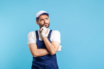 Pensive confused handyman in overalls holding chin, thinking over decision, having suspicion and...
