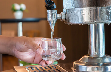 Water is poured into a glass from a manual water dispenser in the hotel restaurant.