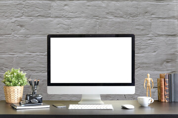 Computer pc with white screen and office equipment on wooden table with stone wall texture background.