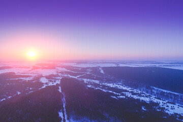Aerial morning view of the countryside. Snowy fields and pine forest at sunrise