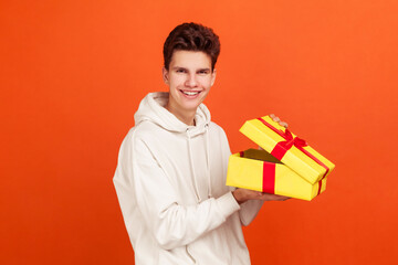 Pleased smiling teenager in casual sweatshirt with hood enjoying holding gift box and looking at...
