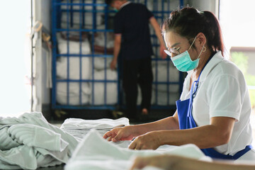 A laundry staff wearing a mask is folding towels with a blurred delivery truck in a background. Shot taken in the factory.