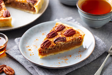 Pecan pie, tart piece on a plate with cup of tea. Grey background. Close up.