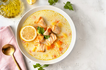 Close up of a plate with delicious salmon soup with vegan cream, carrots and potato on white