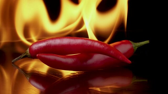 Hot red chili peppers in flames on a black background. Spicy food concept. 4K