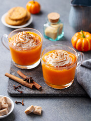 Pumpkin spice latte with whipped cream in glass cups. Grey background. Close up.