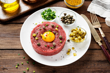 Beef tartare with capers , fresh onion and pickled cucumber on white plate on wooden background.