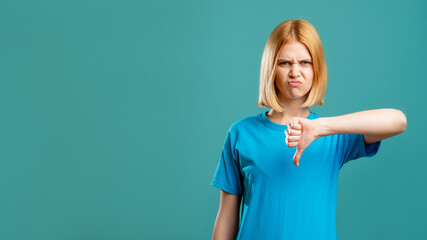 Dislike gesture. Bad idea. Disgusted blonde woman in blue t-shirt showing thumb down isolated on...