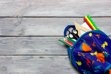 School backpack on light wooden background with stationery