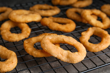 Cooling rack with fried onion rings on grey table, closeup