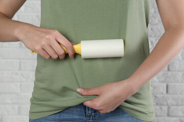 Woman cleaning green t-shirt with lint roller against white brick wall, closeup