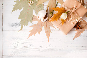 dry maple leaves, gift  white flowers on a white wooden background, copy space