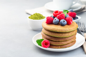Stack of matcha pancakes served blueberry and raspberry on white plate, horizontal, copy space
