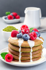 Stack of matcha pancakes served with condensed milk, blueberry and raspberry on white plate, vertical